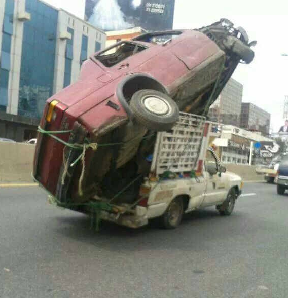 Photo of a small truck overloaded with a bigger pick-up truck in its box